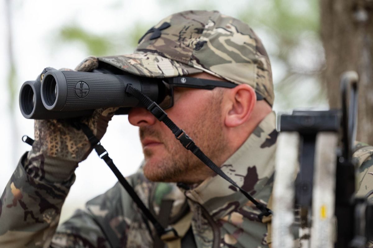 A hunter in camo uses binoculars, choosing lightweight hunting clothes concept.