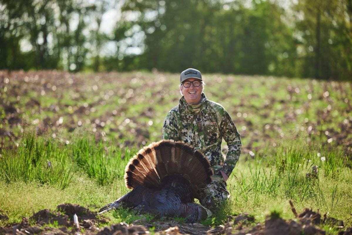 A hunter smiles and poses with a turkey after a successful hunt.