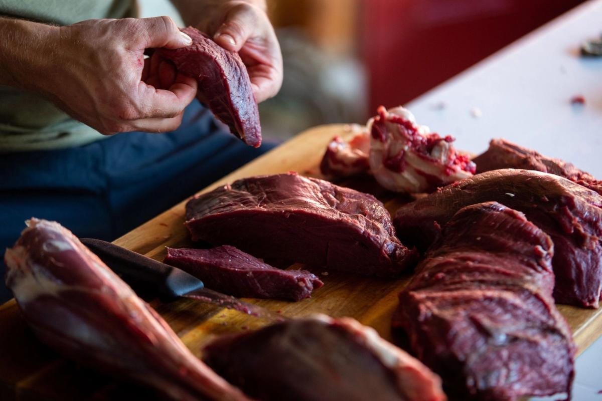 A person handling venison meat on a cutting board, venison dishes concept.