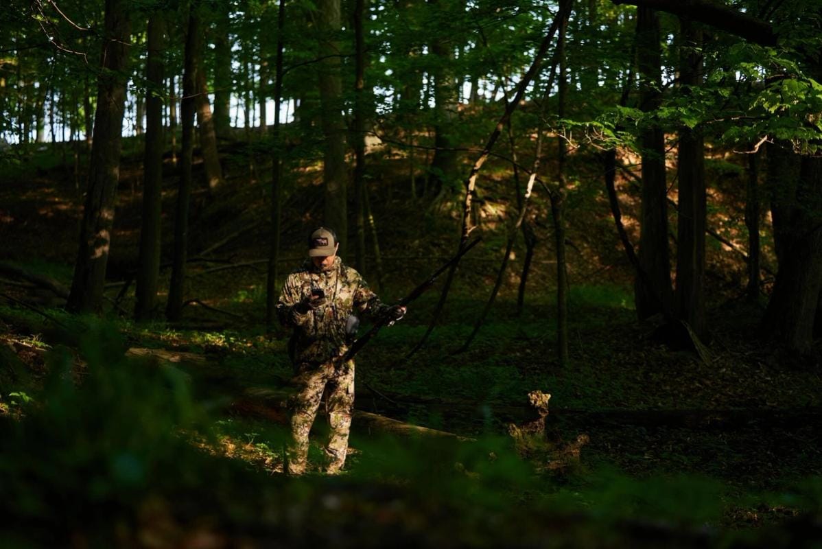 A hunter in the woods looking at a phone, how to find public hunting land near me concept.