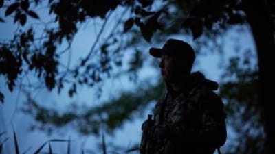 A hunter stands near a tree in the dark, night hunting concept.