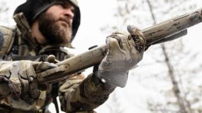 A hunter in camo holds a rifle, understanding hunting shooting positions concept.