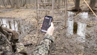 Hand holding phone showing HuntWise near stand, find property lines for hunting concept.