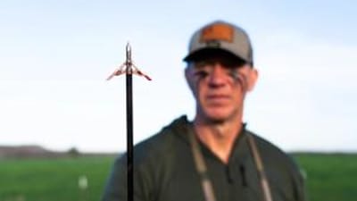 John Dudley blurred behind an arrow in focus, shooting a compound bow concept.