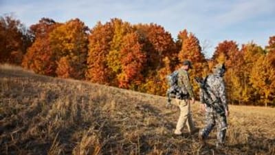 Two hunters walking in field near trees, how to find walk-in hunting in Iowa concept. 
