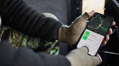 Close-up of hands holding a phone showing the HuntWise hunting weather app on screen.