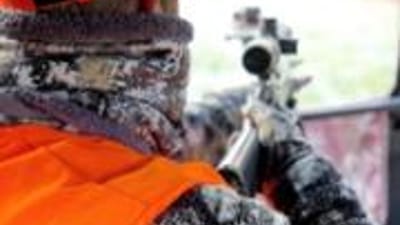 A hunter with gear and bow walks on hunting land.
