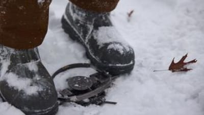 Person setting trap in snow with boots, Michigan trapping season concept.