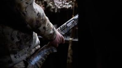 Hunter with shotgun in duck blind, waterfowl shotguns concept.