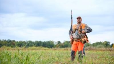 Hunter with shotgun in blaze orange for upland hunt, how to find walk-in hunting in Illinois concept. 