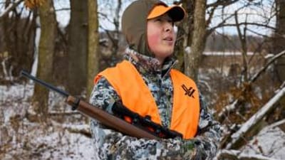 Hunter in blaze orange with rifle, best caliber for small game concept.