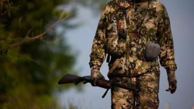 A hunter in camo holding a rifle in the field, get a Mississippi hunting license concept.