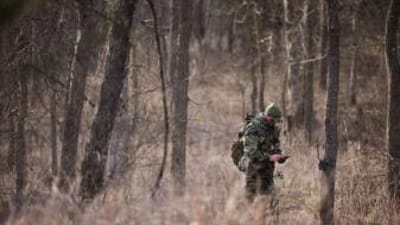 Hunter John Dudley checks phone and trail cam in woods, look for deer hunting land concept.