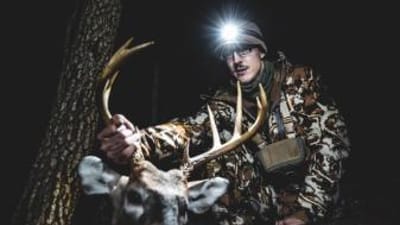 A hunter wearing a head lamp holds up a deer's antlers and head after a hunt, HuntWise app concept.
