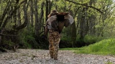 Hunter carrying a turkey on his back in the woods, Wisconsin turkey hunting season concept.
