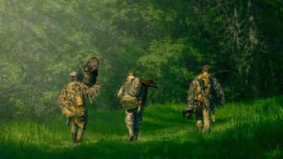 Three hunters from Blueline Bowhunters walking, one carries a turkey, turkey hunting tips concept.