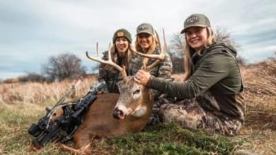 Three women in camo pose with a deer after a kill, find the best hunting time with HuntCast concept.