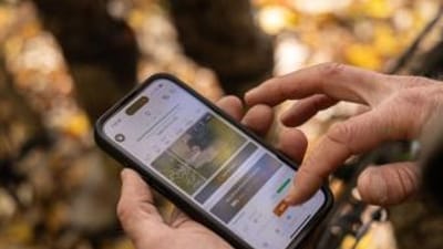 Close-up of a hunter's hands holding a phone and using the HuntWise hunting app.