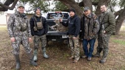 Several hunters gather around a buck in the back of a truck after a hunt.
