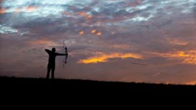 A bowhunter in the distance draws the bow, hunting whitetail deer concept.