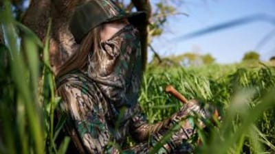 Female hunter uses a slate turkey call in the woods, best turkey calls for beginners concept.