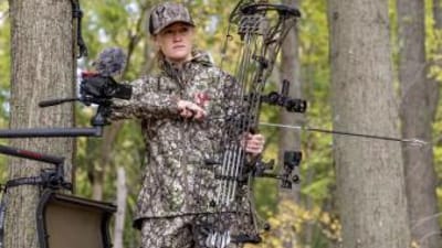 A female hunter in a tree stand gets ready to aim a bow, gun vs. bow shot placement concept.