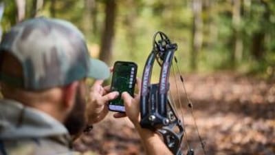 Hunter with bow using phone showing HuntWise on screen, how to use a hunting app concept.