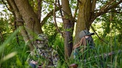 A man and a woman in camo sitting against trees with a shotgun, Osceola turkey hunt concept.