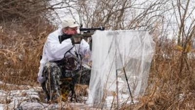 A hunter using a stand in the brush for coyote hunting.