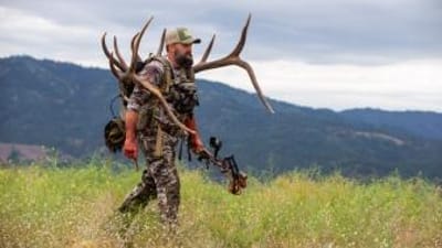 A hunter walks on a ridge carrying a large set of antlers, HuntWise pros concept.