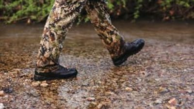Close-up of a hunter's boots as he walks through water, summer huntingn boots concept.