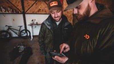 Two hunters looking at a phone, share nearby hunt areas concept.