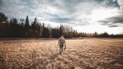 A hunter walks across a field with hunting gear, understanding deer movement concept.