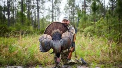 Hunter kneels with turkey after hunt, best caliber for turkey hunting concept.