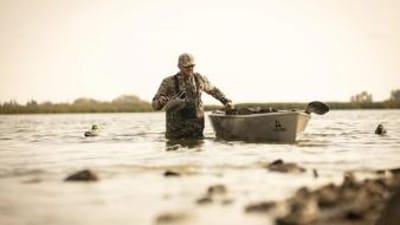 Hunter in waders in the water with canoe setting decoys, best duck hunting equipment concept.