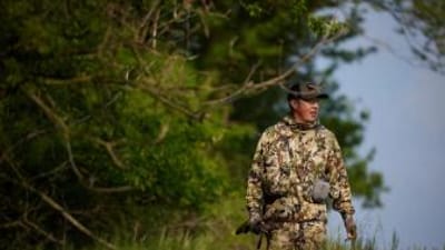 Hunter in camo with firearm walks near trees, how to find walk-in hunting in Kansas concept. 