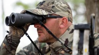 A hunter in camo uses binoculars, choosing lightweight hunting clothes concept.
