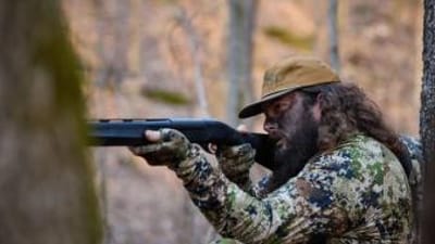 Ben Cole of RootedTV aims a shotgun in the woods, spring hunting concept.