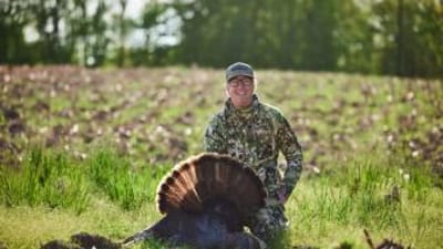 A hunter smiles and poses with a turkey after a successful hunt.