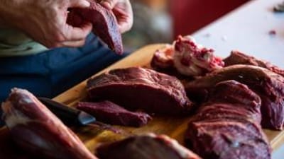 A person handling venison meat on a cutting board, venison dishes concept.