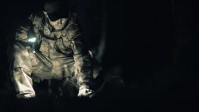 A hunter in camo with a flashlight in the dark, coyote hunting at night concept.