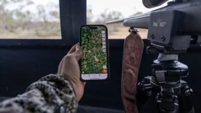 Hunter holds phone showing Huntwise next to rifle in blind, where can I hunt concept.