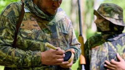 Hunter using turkey call with boy, best turkey hunting gear concept.