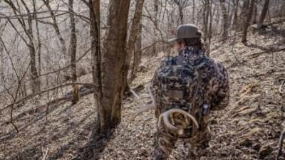 A hunter in the woods wearing a pack with shed antlers attached.