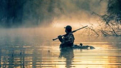 A hunter in the water with a shotgun and waterfowl decoys, best decoys concept.