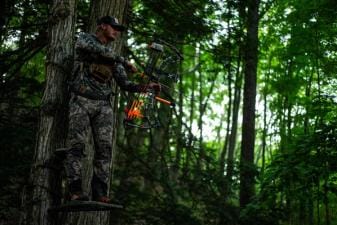 A hunter with a bow wearing camo while in a tree stand, hunt big bucks in thickets concept.