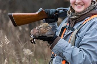 Young hunter with shotgun holds quail, quail hunting tip concept.