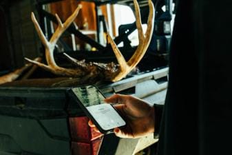 Hunter using HuntWise on phone near deer antlers in back of truck, how to find mule deer concept.