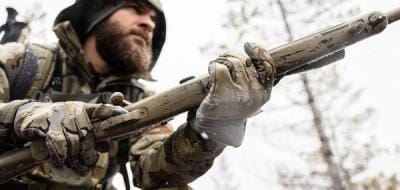 A hunter in camo holds a rifle, understanding hunting shooting positions concept.