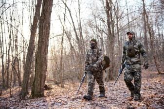 Two hunters in turkey gear walk through the woods, hunt Merriam turkey concept.